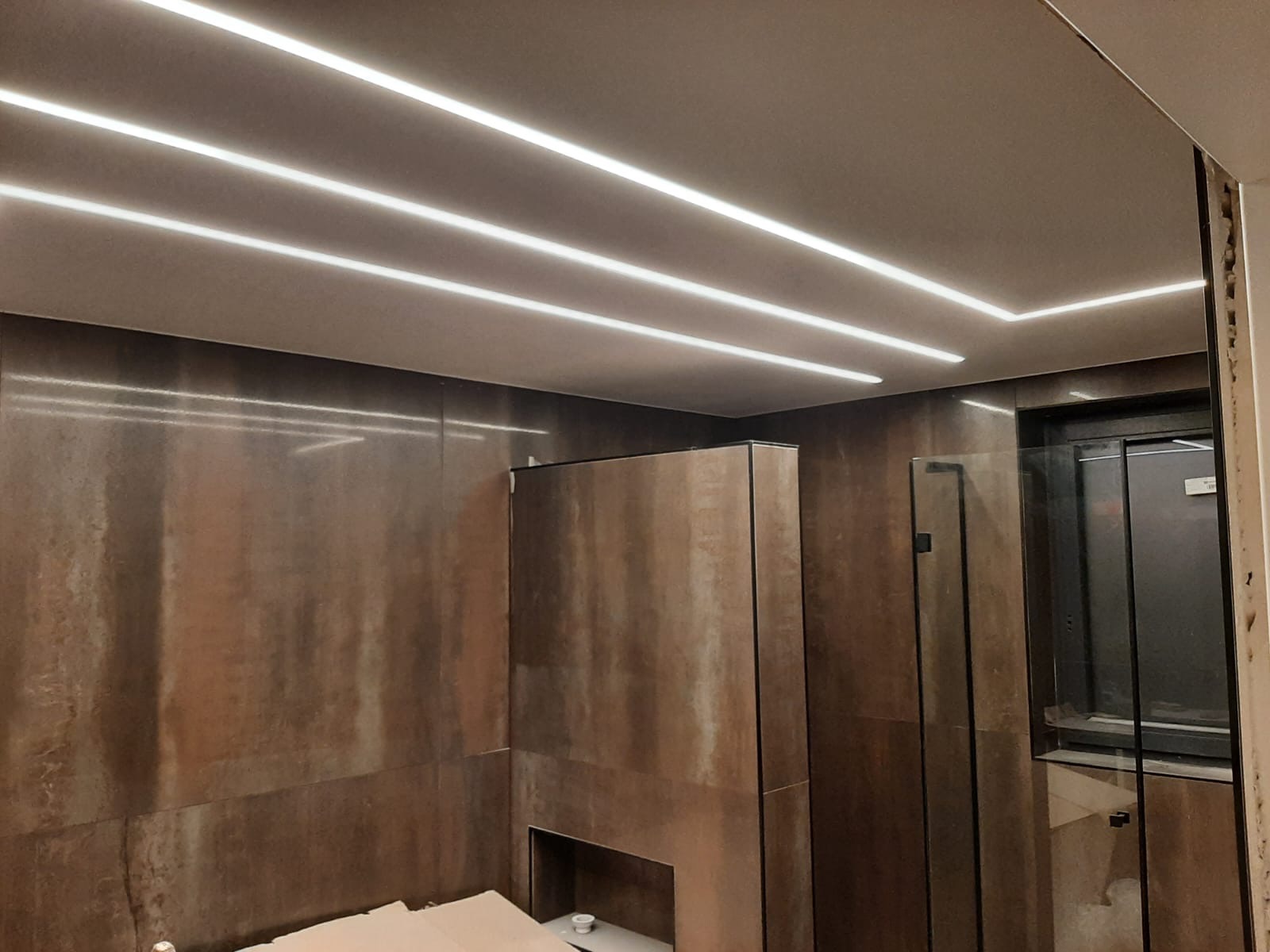 Nowoczesna łazienka z brązowymi płytkami imitującymi rdzę, oświetleniem LED w suficie i minimalistyczną zabudową.