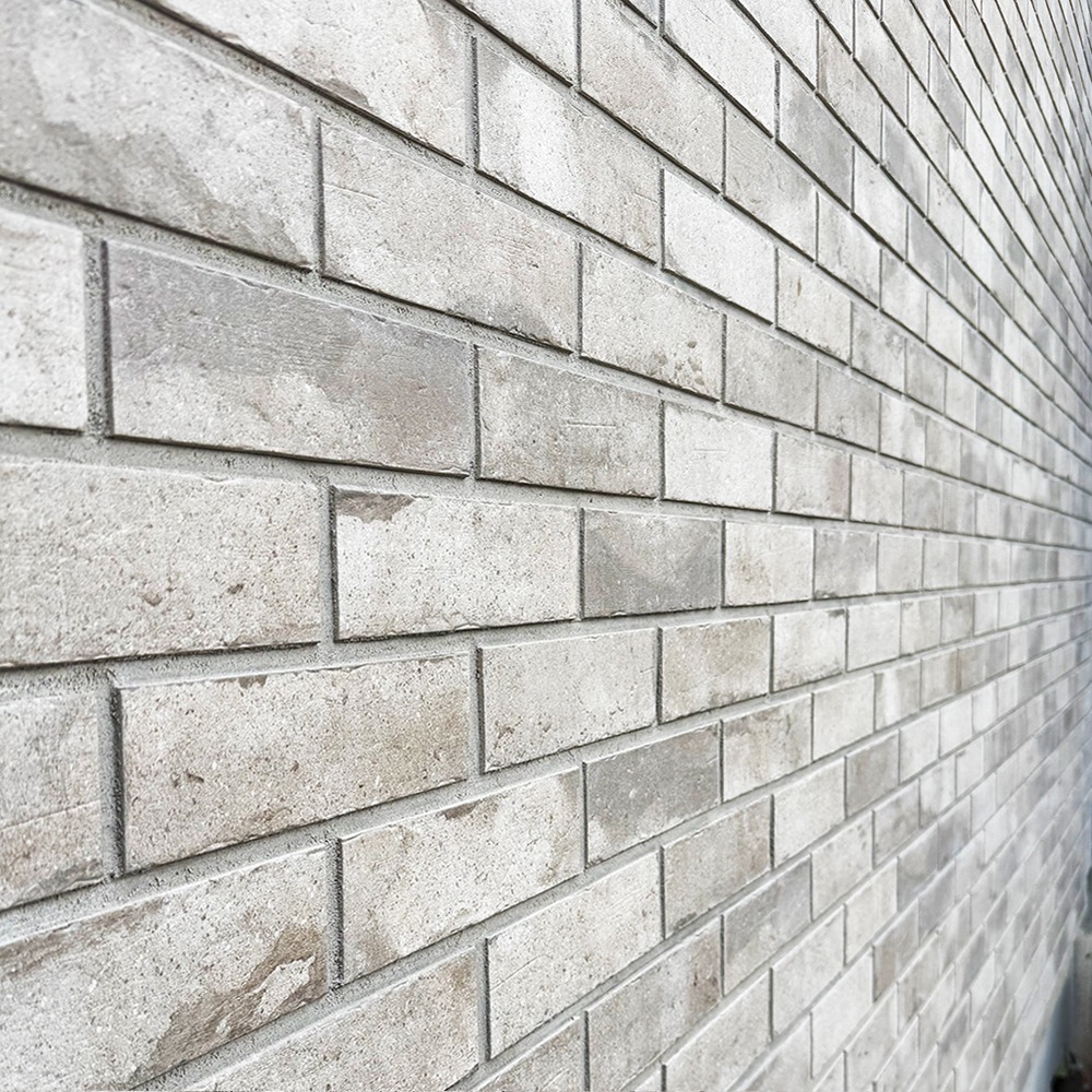 Ściana z szarych, klinkierowych cegieł ułożonych w regularny wzór, widoczna z perspektywy bocznej. Delikatne cieniowanie podkreśla fakturę materiału.