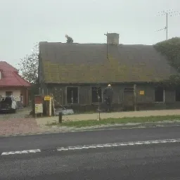 Demontaż starego, drewnianego domu z zarośniętym dachem, dwóch pracowników na dachu i jeden na ziemi, widok z ulicy.