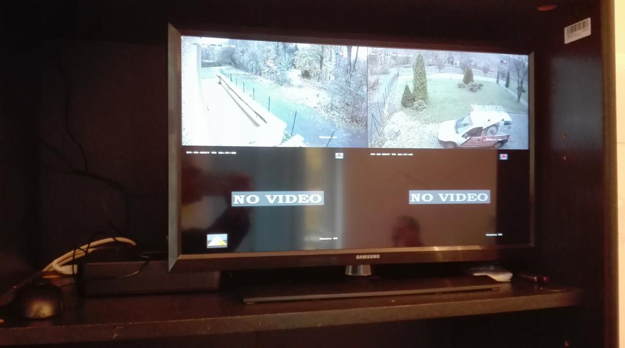 Monitor Samsung wyświetlający podgląd z czterech kamer monitoringu, z dwoma komunikatami 'NO VIDEO', umieszczony na ciemnej półce.
