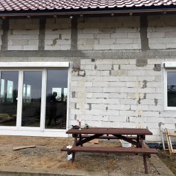 Demonti Karol Prybacki - Montaż okien i rolet zewnętrznych w surowym budynku. Widoczne narzędzia pracy i drabina. Okno trzyskrzydłowe i pojedyncze z zamontowanymi roletami.