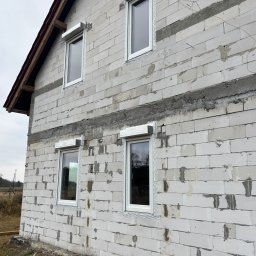 Demonti Karol Prybacki - Surowy budynek z białego bloczka z zamontowanymi oknami i roletami zewnętrznymi w kolorze białym. Widoczne ślady zaprawy i niedokończone wykończenie.