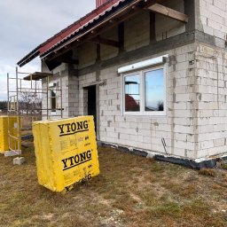 Demonti Karol Prybacki - Budowa domu z białych bloczków Ytong, widoczne rusztowania i zamontowane okno z roletą zewnętrzną. Częściowo ocieplony budynek w trakcie prac wykończeniowych.