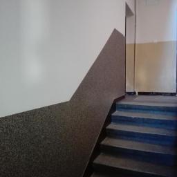 Larem-bud - Klatka schodowa z wykończoną ścianą: dolna część pokryta szorstką, ciemną strukturą w kształcie trójkąta, górna część biała, gładka. Widoczne schody z ciemnego kamienia.