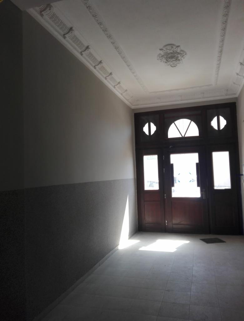 Wnętrze korytarza z odnowionymi ścianami, dekoracyjnym sufitem i drewnianymi drzwiami wejściowymi z przeszkleniami w kształcie półksiężyców.