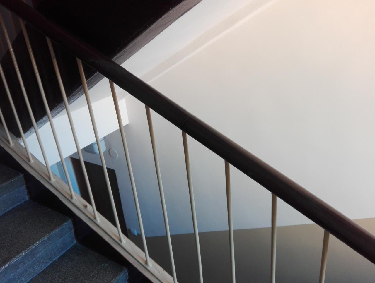 Klatka schodowa po malowaniu: ciemne schody, biała ściana, brązowa poręcz i jasne barierki. Widoczne ślady po wałku na ścianie.