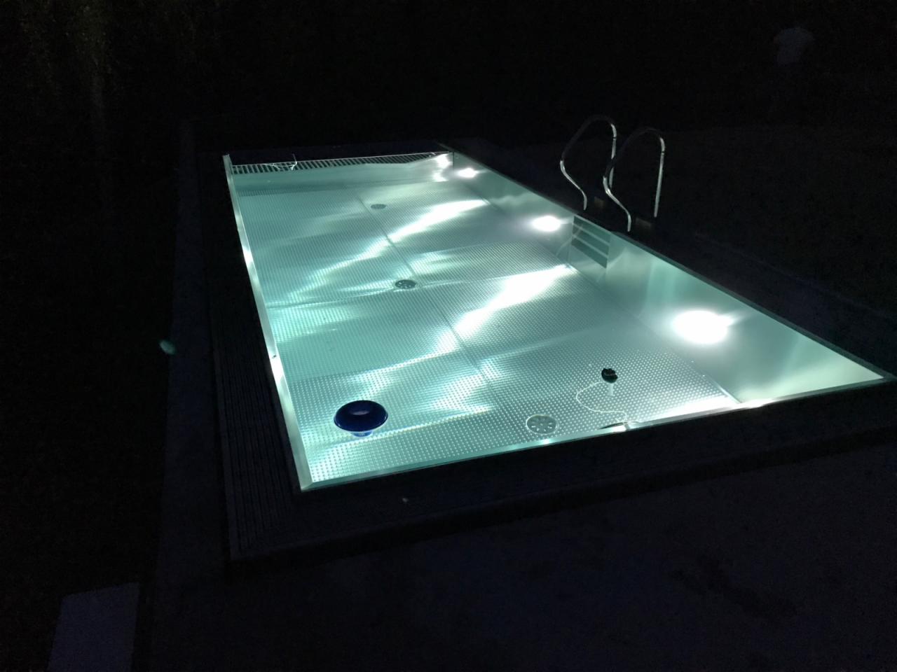 Oświetlony basen z drabinką widziany nocą, z widocznym niebieskim elementem czyszczącym na dnie.