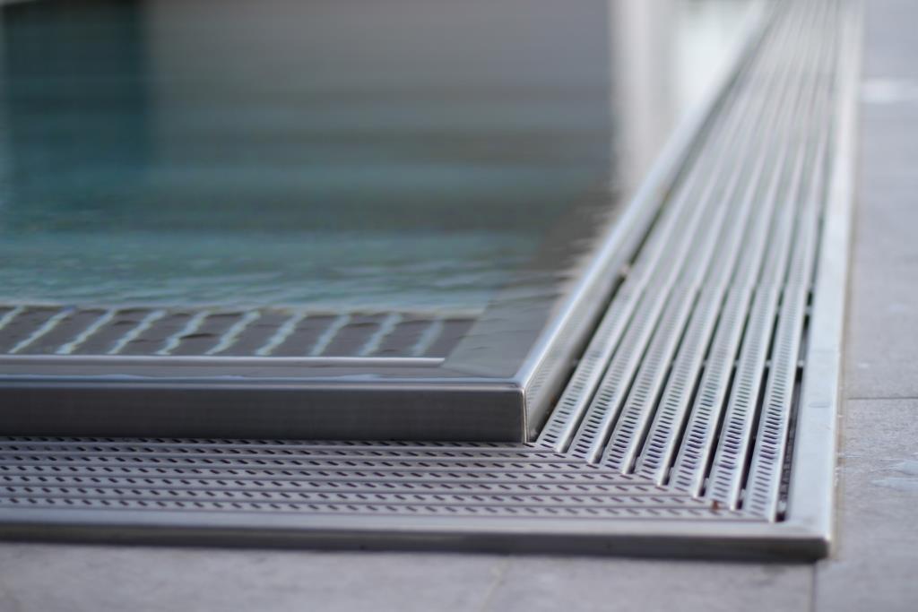 Minimalistyczne ujęcie krawędzi basenu z metalowym wykończeniem i odpływem liniowym, woda lekko faluje.