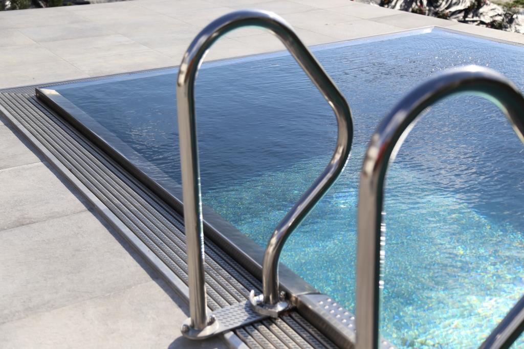 Nowoczesny basen z metalową drabinką i ukrytą pokrywą, otoczony jasnymi płytami chodnikowymi.