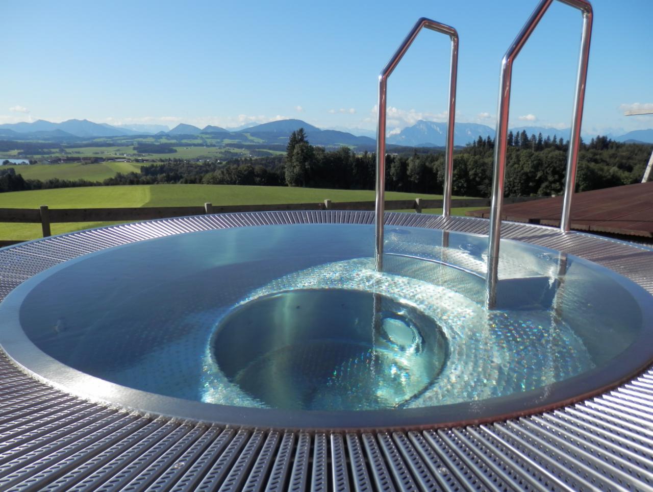 Okrągły basen z metalową obudową i drabinką, w tle zielone wzgórza i góry pod błękitnym niebem.