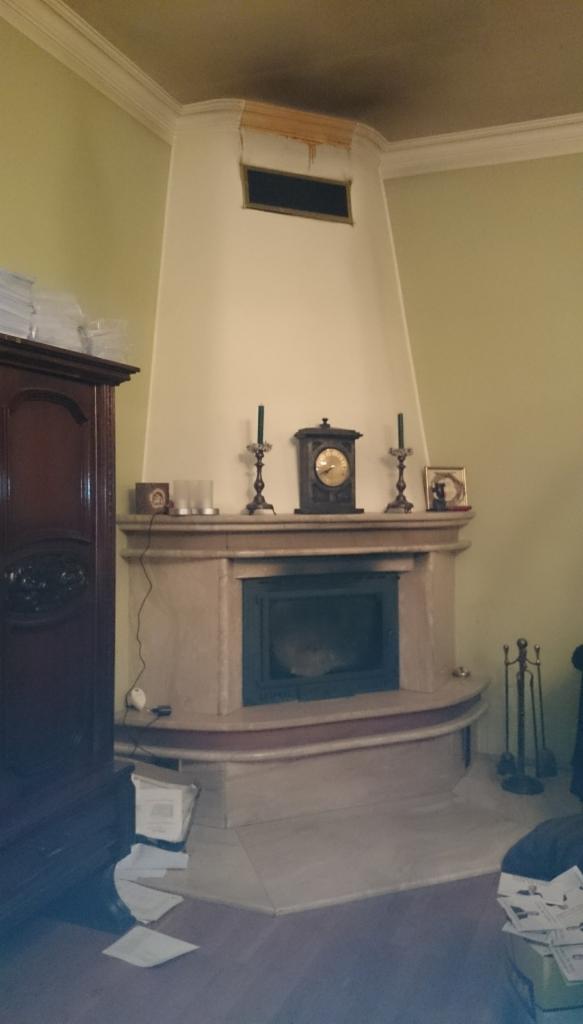 Klasyczny, marmurowy portal z wkładem, zwieńczony półką z zegarem i świecznikami, z widocznym uszkodzeniem sufitu nad nim.