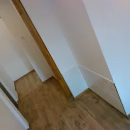 Korytarz w domu z drewnianą podłogą, białe ściany, fragment ściany wyłożony białą, poziomą cegiełką i drewniana belka stropowa.