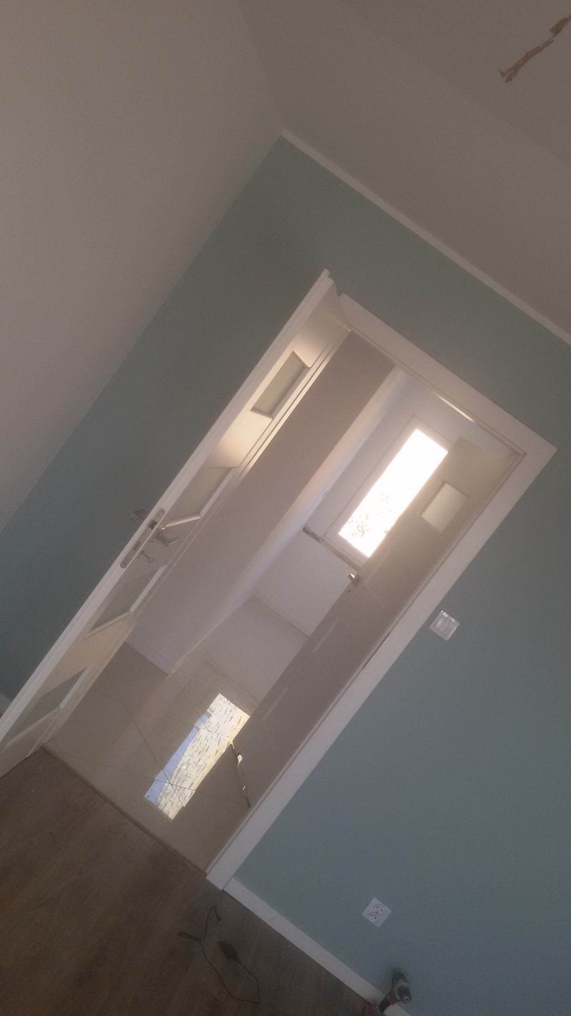 Białe drzwi z przeszkleniami, zamontowane w ścianie pomalowanej na jasny odcień koloru niebieskiego, widok z dołu pod kątem, widoczny fragment podłogi i sufitu.