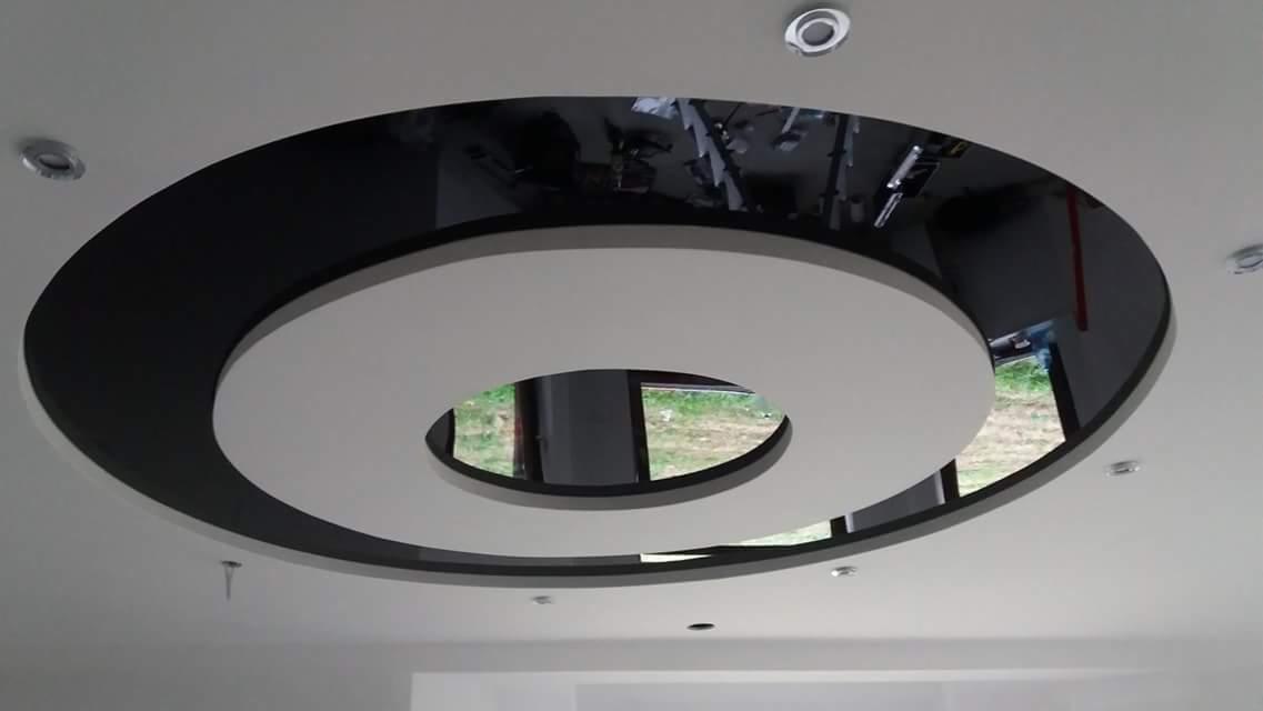 Oryginalny, dwukolorowy sufit podwieszany z okrągłymi elementami i punktowym oświetleniem w Czeladzi, z widocznym odbiciem drabiny malarskiej.