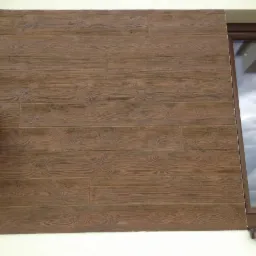 Fragment elewacji budynku z brązowymi panelami imitującymi drewno, widoczny fragment okna z odbiciem chmur.