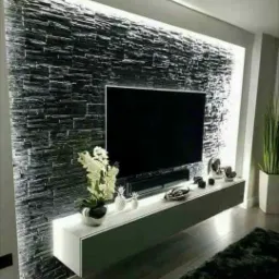 Czarna ściana z kamienia dekoracyjnego z podświetleniem LED za telewizorem, uzupełniona białym, wiszącym stolikiem RTV z dekoracjami.
