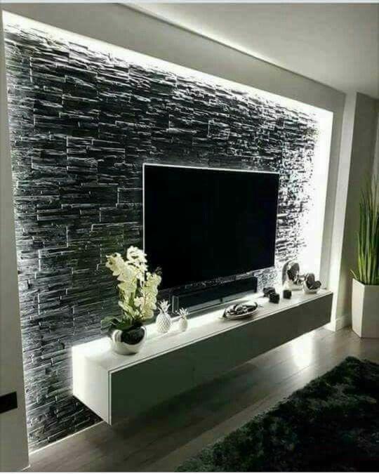 Czarna ściana z kamienia dekoracyjnego z podświetleniem LED za telewizorem, uzupełniona białym, wiszącym stolikiem RTV z dekoracjami.