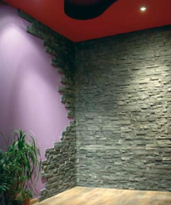 Wnętrze z częściowo wykończoną ścianą z szarego kamienia dekoracyjnego, odsłaniającą fioletową ścianę pod spodem, z rośliną doniczkową w rogu i czerwonym sufitem z czarnym elementem dekoracyjnym.