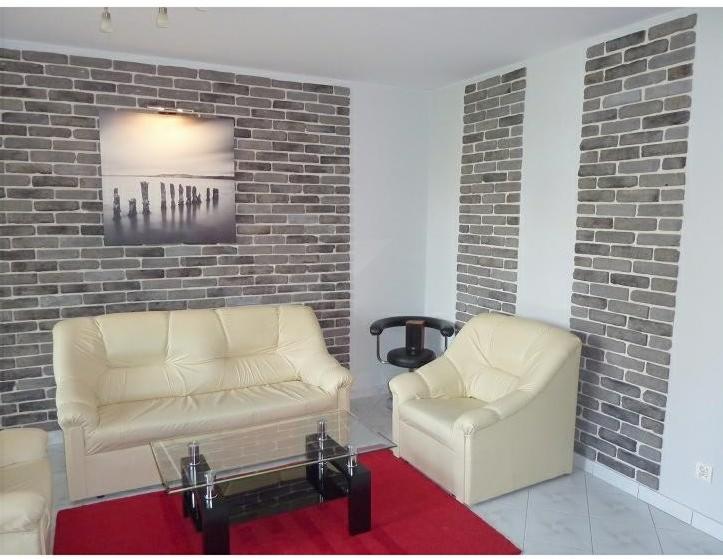 Salon z dekoracyjną ścianą z szarej cegły, kremowa sofa, fotel i czerwony dywan, obraz nad sofą.