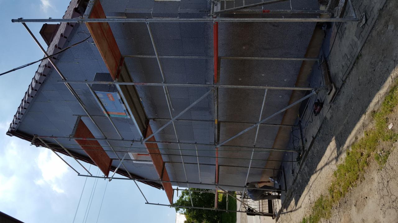 Dom w trakcie ocieplania styropianem grafitowym, widoczne rusztowanie i pracownik przy elewacji.