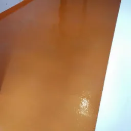 Błyszcząca, pomarańczowa podłoga z żywicy epoksydowej, widoczne odbicie światła i fragment ściany.