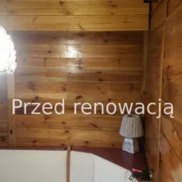 Pokój wyłożony boazerią przed renowacją, widoczny narożnik z sofą, lampka nocna i stół z fioletowym obrusem.
