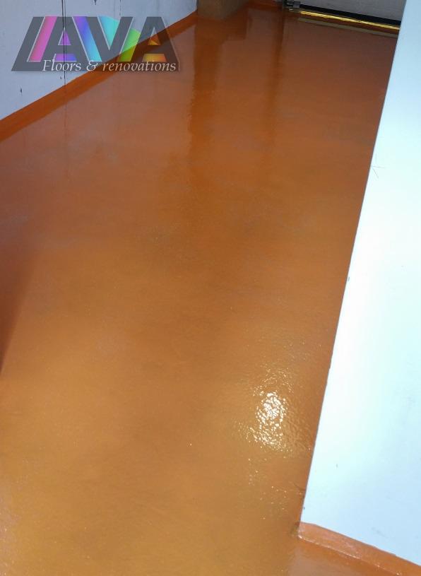 Błyszcząca, pomarańczowa podłoga z żywicy epoksydowej, widoczne odbicie światła i fragment ściany.