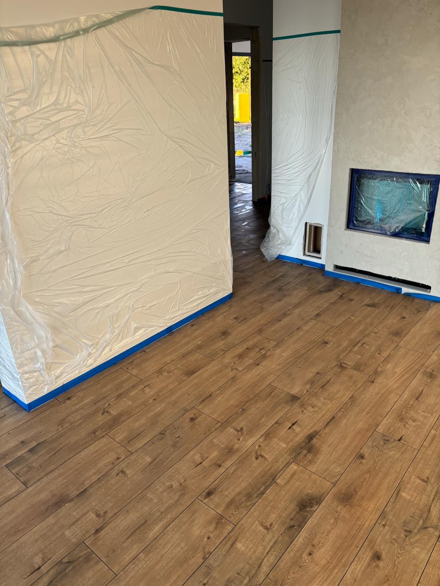 Pokój zabezpieczony folią i taśmą malarską przed malowaniem lub innymi pracami wykończeniowymi, widoczna drewnopodobna podłoga.