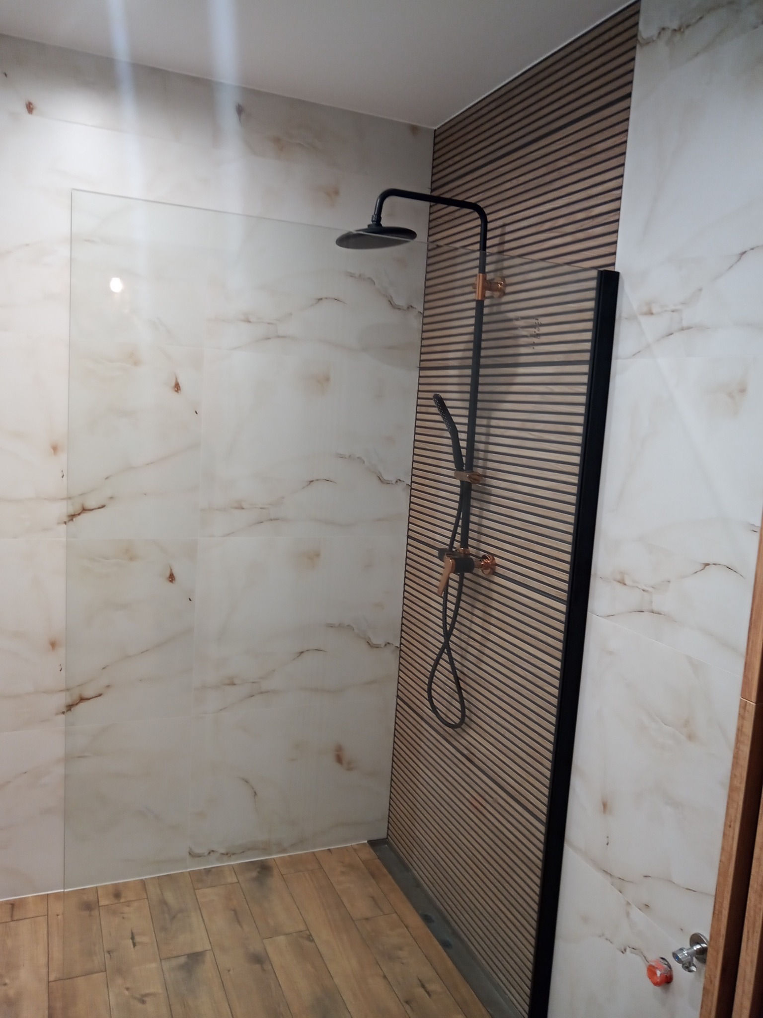 Wykończona kabina prysznicowa z czarną armaturą na tle ściany z paneli dekoracyjnych i marmuropodobnych płytek.