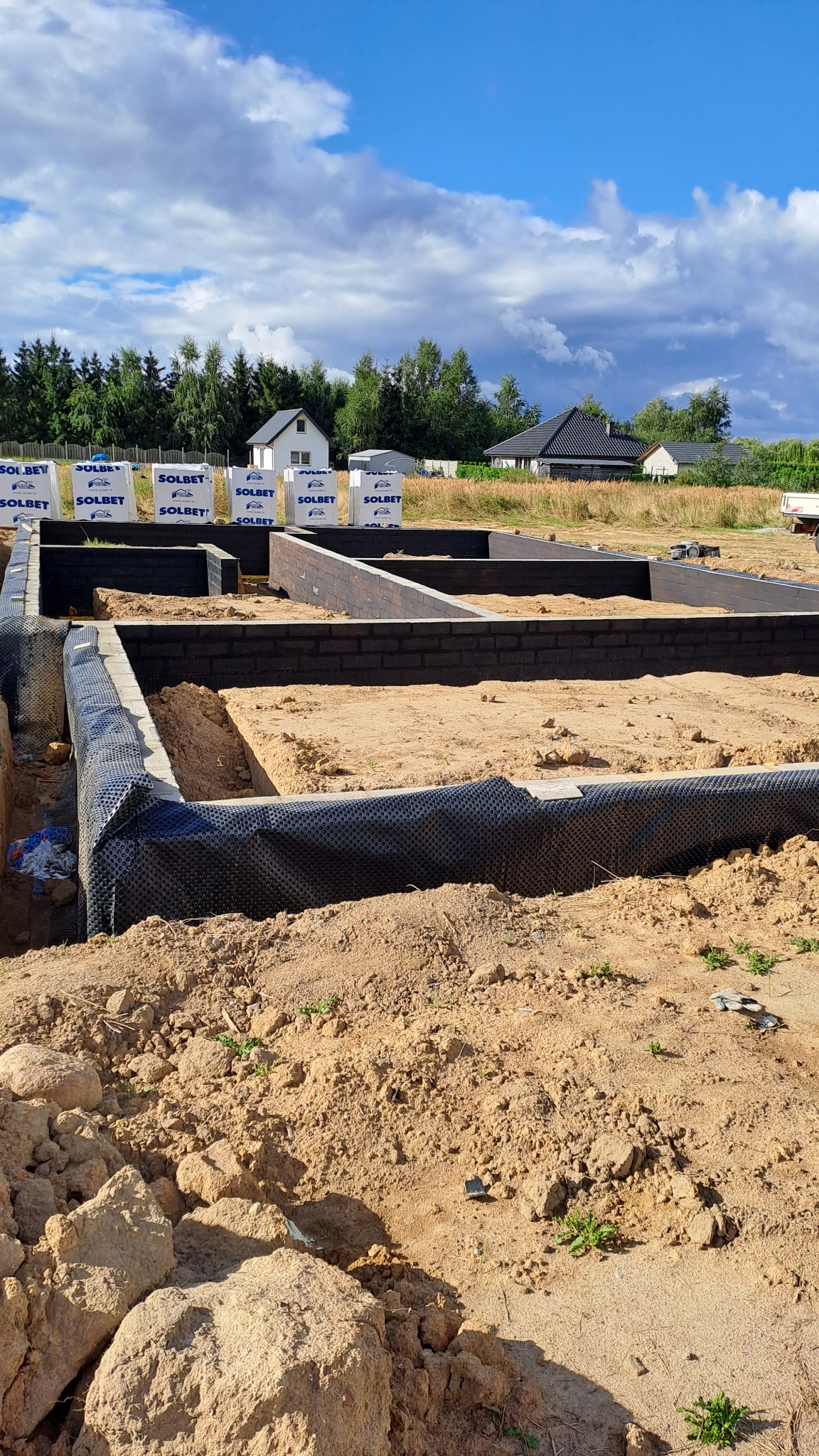 Wykop pod fundamenty domu jednorodzinnego, zabezpieczony czarną folią izolacyjną, widoczne bloczki Solbet i przygotowany teren pod budowę.