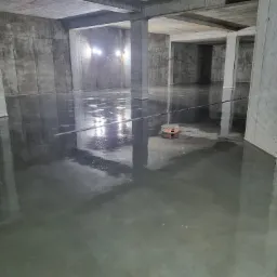 Świeżo wylana, gładka posadzka w surowym wnętrzu w Choruli, z widocznymi kolumnami i lampami budowlanymi.