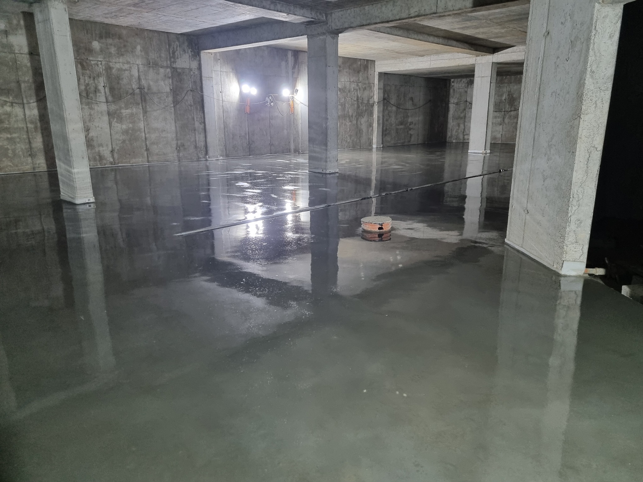 Świeżo wylana, gładka posadzka w surowym wnętrzu w Choruli, z widocznymi kolumnami i lampami budowlanymi.