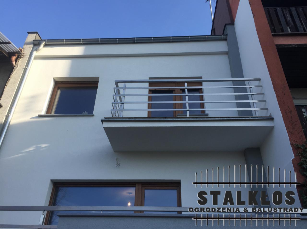 Biała elewacja budynku z balkonem zabezpieczonym nowoczesną, metalową balustradą; widoczny fragment logo firmy specjalizującej się w balustradach.