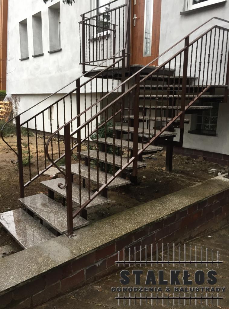 Zewnętrzne schody z szarego granitu z brązową metalową balustradą, prowadzące do drzwi wejściowych domu.