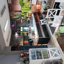 Wnętrze lokalu gastronomicznego z ladą chłodniczą, stolikami z białymi krzesłami i menu wypisanym kredą na tablicy.