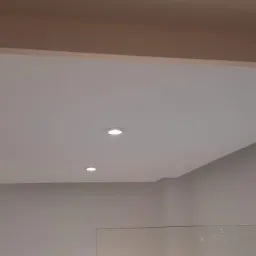 Podwieszany sufit z płyt kartonowo-gipsowych, z wbudowanymi, okrągłymi lampami LED, wykończony gładzią i pomalowany na biało, widok z dołu.