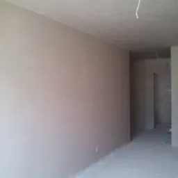 Wnętrze pokoju po nałożeniu gładzi gipsowej, widoczny sufit z wystającym przewodem elektrycznym, wiadro po farbie w rogu pomieszczenia.