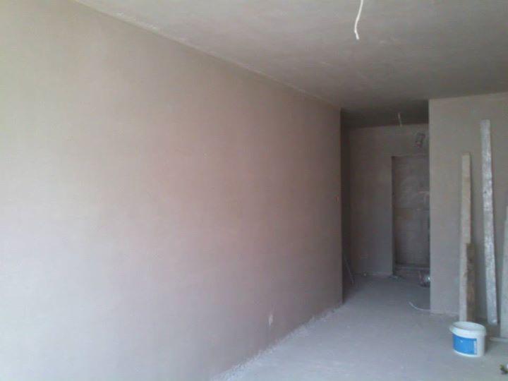 Wnętrze pokoju po nałożeniu gładzi gipsowej, widoczny sufit z wystającym przewodem elektrycznym, wiadro po farbie w rogu pomieszczenia.