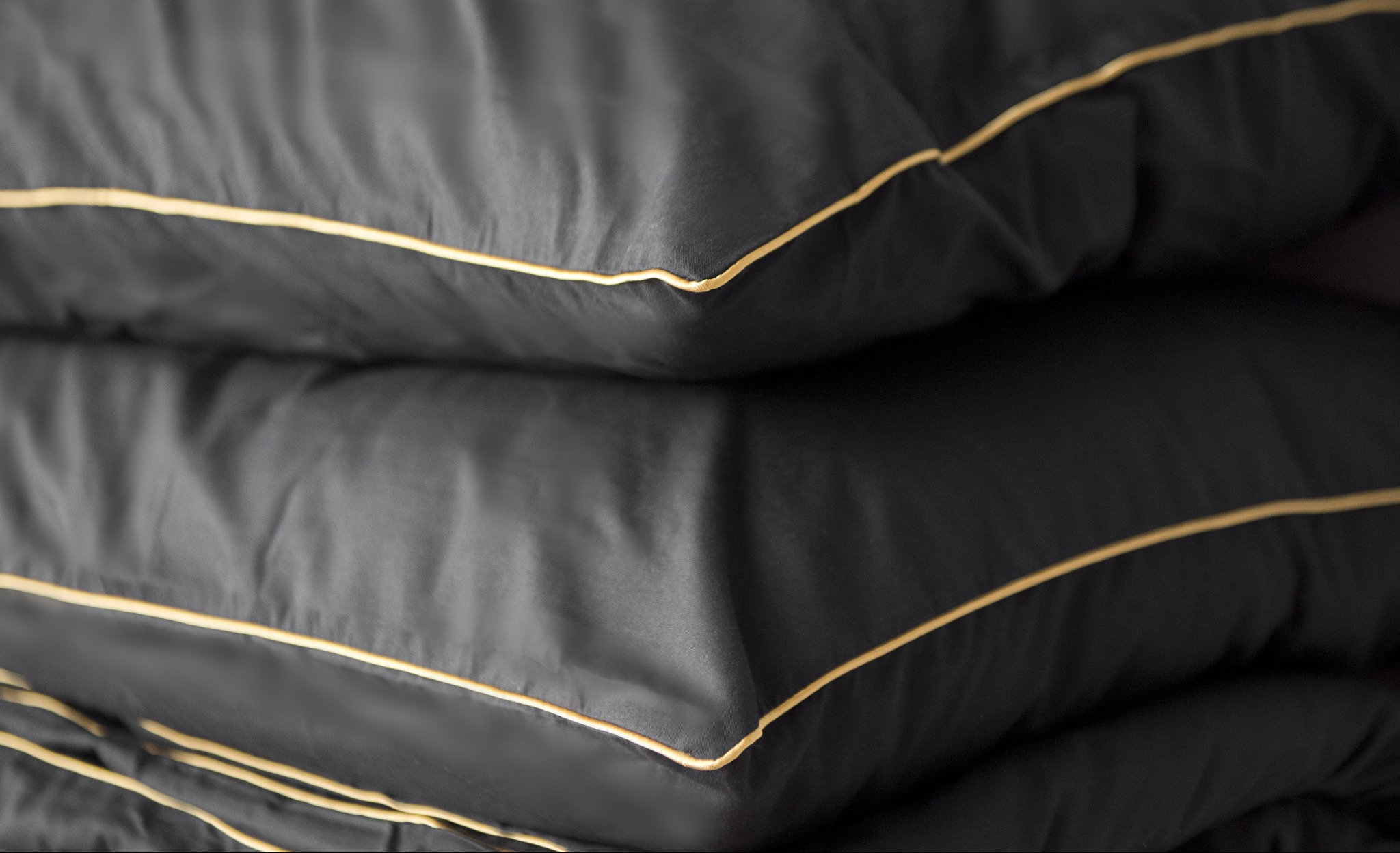 Stos czarnych poduszek z ozdobną, złotą lamówką, ukazujący precyzję szycia i dbałość o detale. Gładka tkanina i staranne wykończenie podkreślają wysoką jakość produktu.