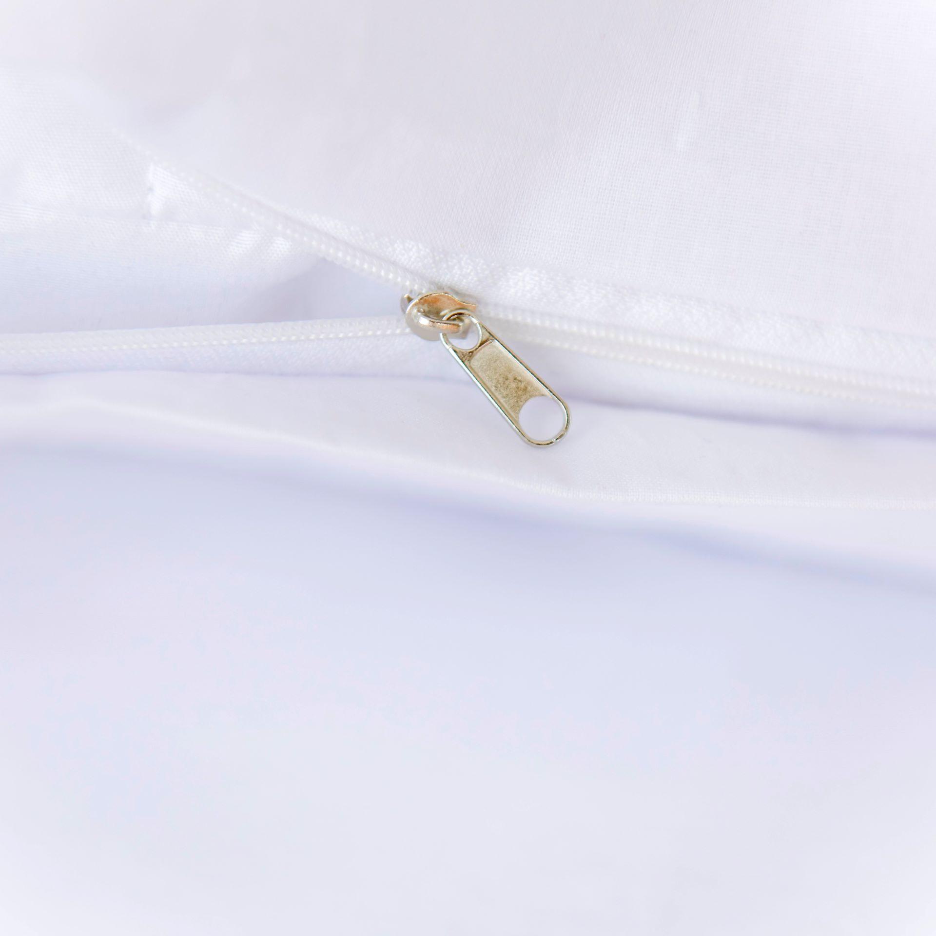 Biała poszewka na kołdrę z metalowym suwakiem, widoczne delikatne marszczenia materiału i faktura tkaniny. Ujęcie z bliska, skupione na detalu.