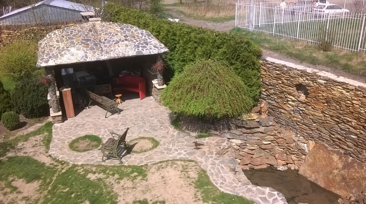 Widok z góry na kamienną altanę z mozaikowym dachem, kamienną ścieżkę, mur z kamienia łupanego i niewielki strumień w ogrodzie.