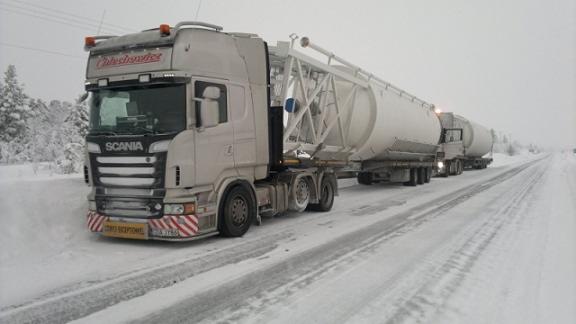 Ciężarówka Scania z naczepą cysterną przewożąca ładunek w zimowych warunkach, na ośnieżonej drodze.