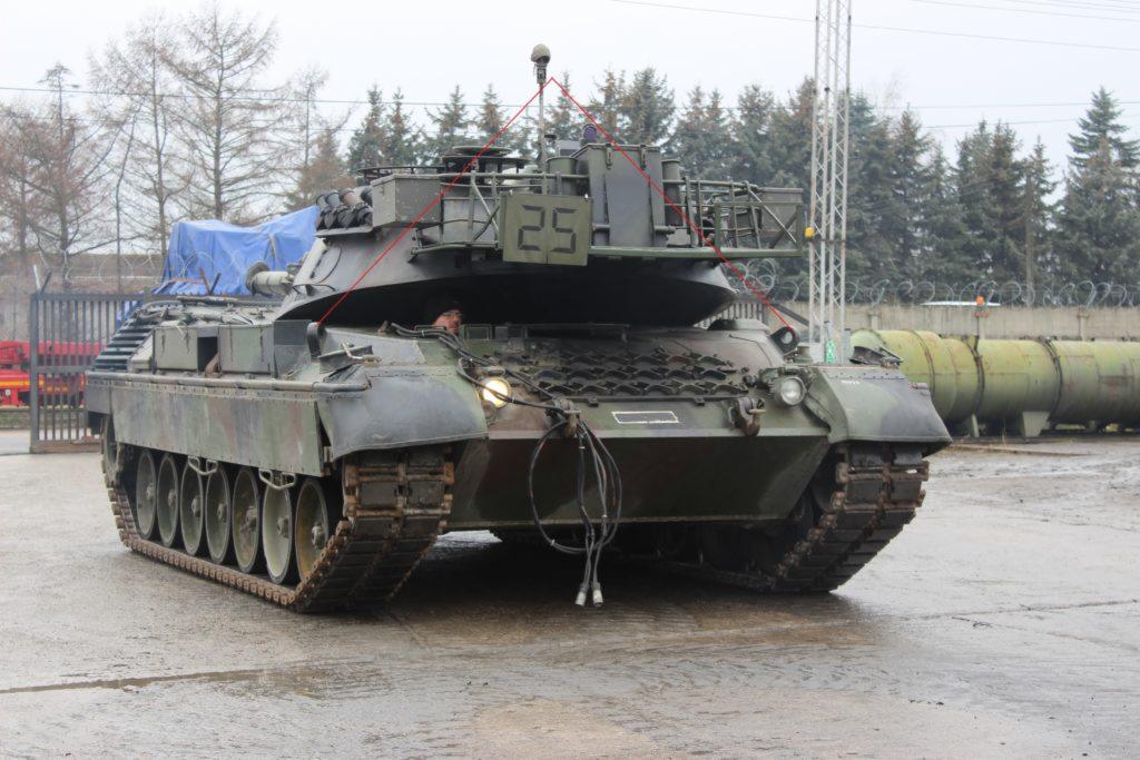 Czołg Leopard 1 w kamuflażu, z numerem 25 na wieżyczce, przewożony na lawecie, widok z przodu, z widocznymi kablami i przewodami.