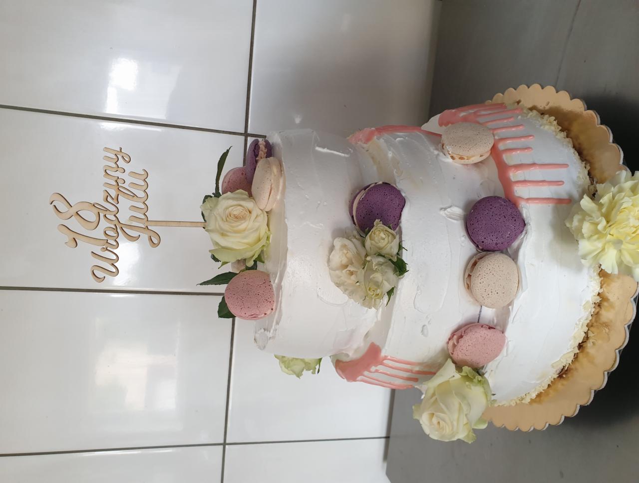 Trzypiętrowy tort urodzinowy z białym kremem, zdobiony makaronikami w pastelowych kolorach, świeżymi różami i drewnianym topperem z napisem '18 Urodziny Julii'.