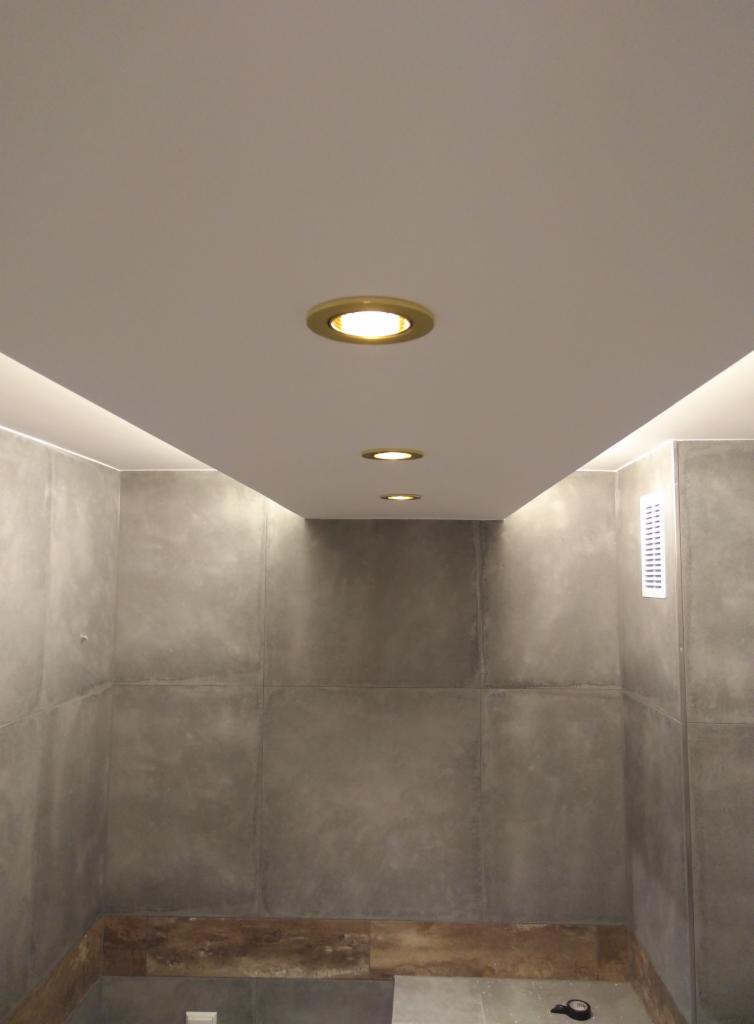Wykończona łazienka z szarymi płytami imitującymi beton, oświetleniem punktowym w suficie i listwą LED.