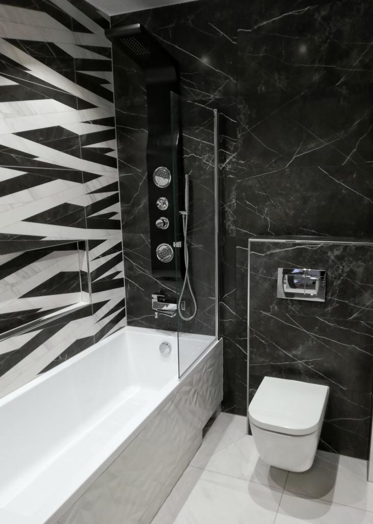 Nowoczesna łazienka w czarno-białej kolorystyce z wanną obudowaną srebrną mozaiką, czarnym panelem prysznicowym z hydromasażem i toaletą wiszącą.