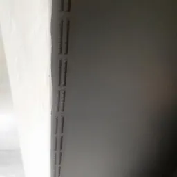 Świeżo pomalowany sufit w odcieniach szarości z kratką wentylacyjną, zabezpieczony folią malarską.