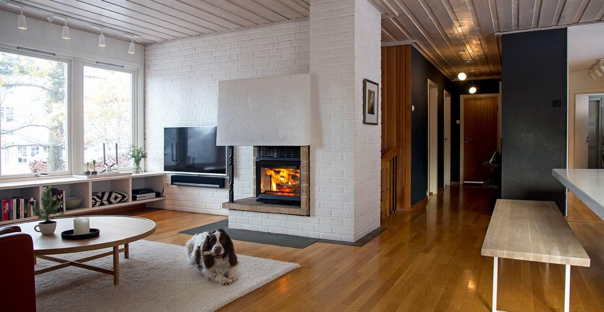 Jasne wnętrze salonu z ceglanym kominkiem z paleniskiem, drewnianą podłogą i psem leżącym na dywanie.