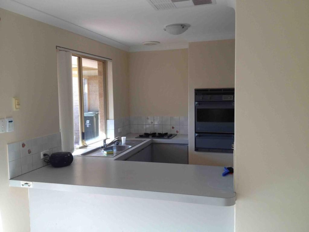 Kuchnia w trakcie remontu: widok na blat, zlew i okno, z zabudowanym piekarnikiem w tle, ściany w jasnym odcieniu beżu.