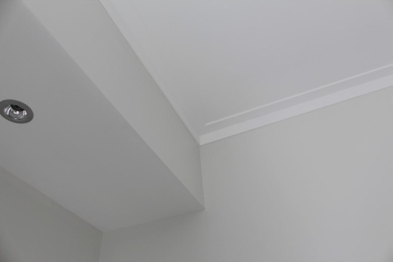 Jasnoszary sufit z zamontowanym halogenem i dekoracyjną listwą przysufitową w narożniku pomieszczenia.